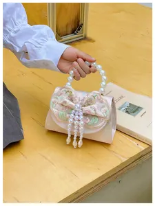 Detail of pink embroidered handbag featuring 3D bow, pearl handle, and elegant fringe