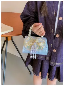 Detail of light blue kids handbag with pearl fringe, lace bow and embroidery