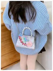 Détail d'un sac bandoulière pour fille avec fleurs et poignée en perles porté par un enfant