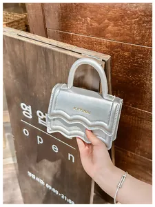 Détail du mini sac argenté avec rabat à bords festonnés et poignée sur le dessus