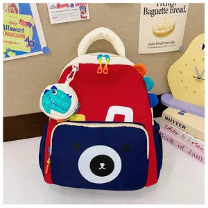 Close-up of kids dinosaur backpack featuring a cartoon bear pocket and red blue color block