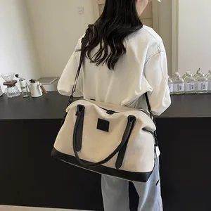 Detail of a beige canvas travel tote with black leather trim and adjustable shoulder strap