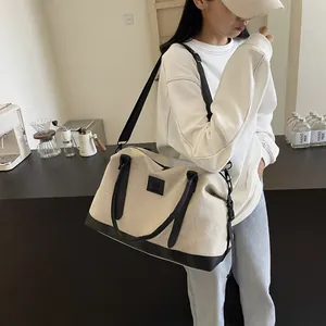Detail of canvas travel bag with leather handles and adjustable shoulder strap worn by model