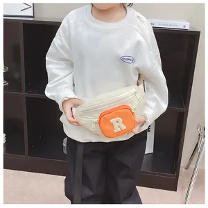 Close-up of kids' cream chest bag with orange zipper pocket and R patch detail
