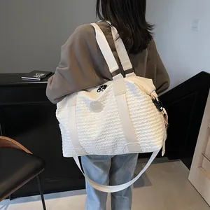Detail of white quilted travel bag with large capacity and woven shoulder straps shown on model