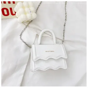 Détail d'un mini sac blanc avec rabat ondulé, lettrage doré et bandoulière chaîne