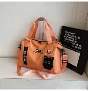 Detail of orange travel bag with cat logo, plush pendant and adjustable shoulder strap