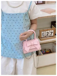 Detail van roze handtas met strik en zilveren ketting gedragen door een model