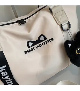 Detail of beige travel bag with cute cat ear embroidery and plush cat head charm