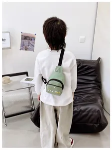 Vue arrière d'un enfant portant un sac bandoulière vert clair avec lettres KAYINAI
