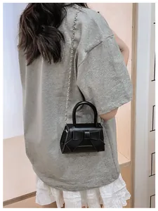 Detail van een zwarte mini-tas met strik en zilveren ketting gedragen door een model