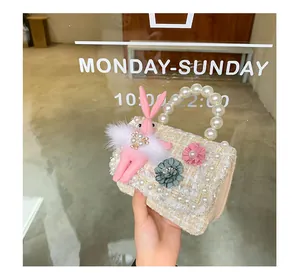 Close-up of girls' tweed handbag with pearl handle, floral decor and plush bunny toy