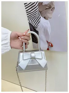 Detail van de zilveren metallic handtas met strik en een metalen ketting schouderband