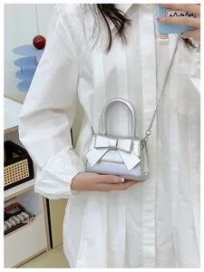 Detail van een zilveren mini crossbody tas met strik en metalen ketting op model