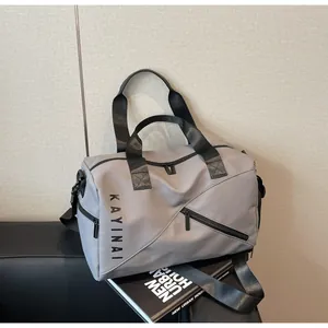 Vista lateral de bolsa de viaje gris con logo Kayinai negro y bolsillo frontal con cremallera