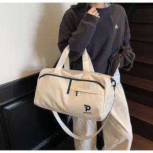 Detalle de un bolso de viaje beige con letras negras y correa de hombro ajustable