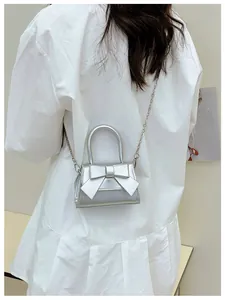 Detail van de zilveren mini-tas met strik, metallic afwerking en dunne kettingriem