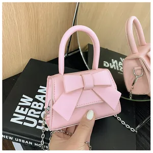 Detail van roze mini-handtas met strik en zilveren ketting op een boek