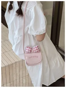 Detail of pink crossbody bag for kids featuring a plaid bow and embossed lettering