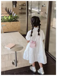 Close-up of pink mini crossbody bag with plaid bow and cat print detail on white dress