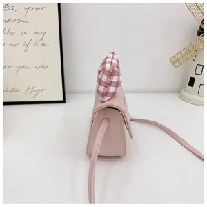 Side view of a pink mini crossbody bag with a decorative red checkered bow and strap