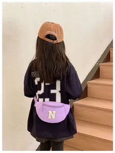Toddler wearing a purple waist bag with letter N patch while standing on wooden stairs