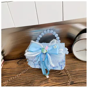 Détail d'un sac à main bleu clair pour enfant avec paillettes, nœud en dentelle et perles