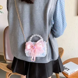 Sac perle pour fille avec nœud rose et bandoulière dorée présenté dans un décor de vie