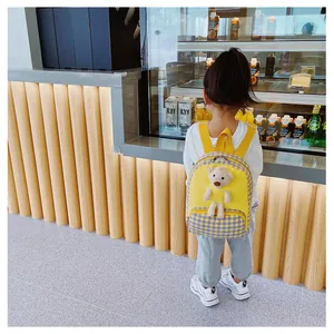 Kid wearing yellow and purple checkered backpack with a 3D plush bear in a retail store