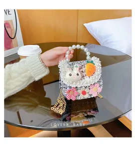 Detail of woven kids bag with pearl handle, plush bunny, and floral charms on black table