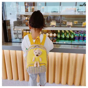 Macro detail of toddler backpack featuring yellow fabric and plush teddy bear ornament