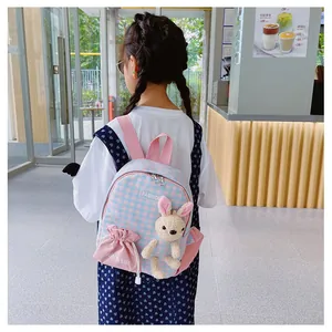 Rear view of a girl wearing a pink and blue plaid toddler backpack with a plush bunny charm