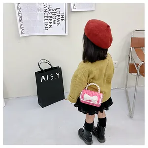 Pink tweed kids handbag with pearl handle and white bow detail shown on a model
