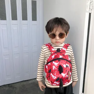 Toddler red cartoon dinosaur backpack with 3D fins shown worn by a child outdoors