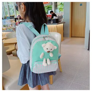 Toddler modeling a mint green bunny backpack with plaid pocket and plush bear in a cafe