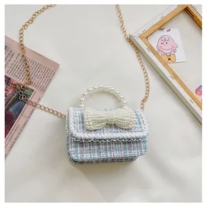 Detail of tweed crossbody bag featuring pearl bow ornament and gold chain strap