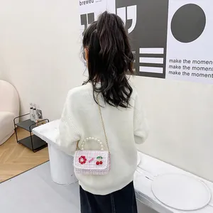 Pink tweed kids crossbody bag with pearl handle and cherry charms shown in a lifestyle scene