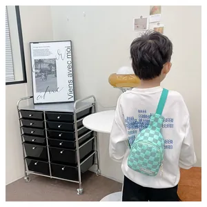 Detail showing checkered green kids chest bag with adjustable strap on white sweater