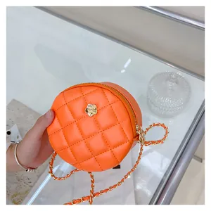 Detail of orange round quilted crossbody bag with a gold flower and woven chain strap