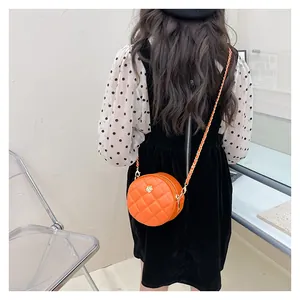 Detail of child wearing an orange quilted round crossbody bag with gold flower emblem