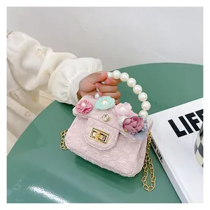Detail of pink girls handbag featuring flower ornaments, pearl handle and gold chain
