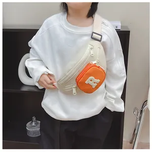 Close-up of cream crescent chest bag with orange square pouch and plush R letter charm