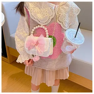 Detail of child handbag with pearl handle, pink bow and fuzzy ball charm on girl