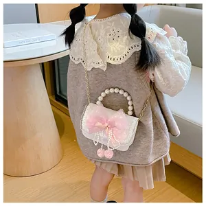 Detail of child handbag showing pink bow, lace texture, pearl handle and pompom charms