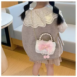 Girl wearing a white lace crossbody bag with pink bow, pearl handle and gold chain