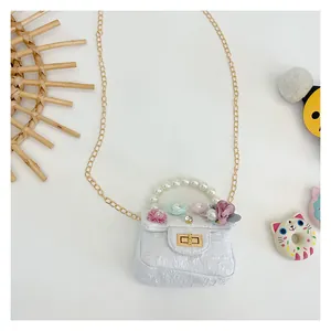 Close-up of white mini girls bag with pearl handle, floral decor, and gold chain strap