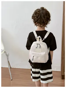 Petit enfant portant un sac à dos en nylon crème, vue de dos dans un décor épuré