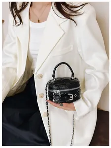 Detail van zwarte gewatteerde mini-tonvormige tas met zilveren ketting op witte blazer