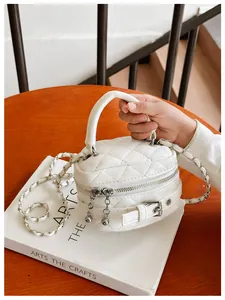 Detail van de witte gewatteerde mini-handtas met dubbele ritsen en een zilveren ketting