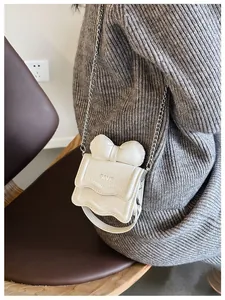 Close-up of white mini crossbody bag with bow detail and silver chain strap on model